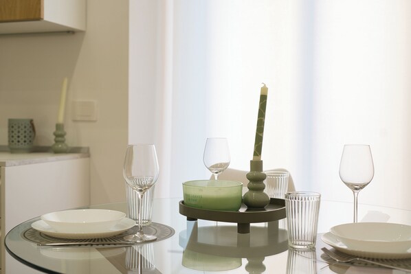 A dining table with a candle, glasses, and plates, set against a window with curtains. - Mascari Suites - Saxum (Lecco)