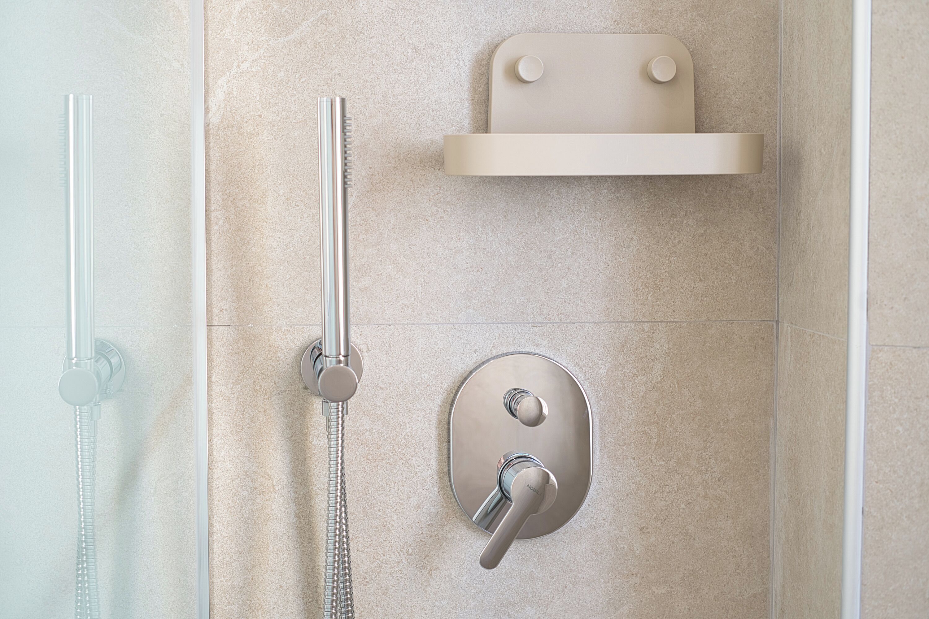 Una ducha moderna con cabezal de ducha de mano, panel de control en la pared y zona de ducha con mampara de vidrio.