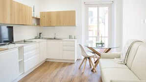A modern kitchen with white cabinetry, a dining area with a glass table and chairs, and a sofa with a blanket. - Mascari Suites - Saxum (Lecco)