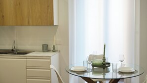 A modern kitchen with a wooden cabinet, a glass dining table set with plates, glasses, and a candle. - Mascari Suites - Saxum (Lecco)