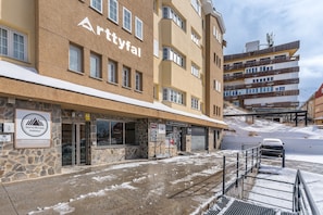 Um hotel com fachada de pedra, várias varandas e um estacionamento com o chão coberto de neve.