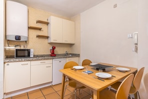 A compact kitchen with a microwave, red coffee maker, and a dishwasher. There is a wooden dining table with chairs and a small cabinet above it.