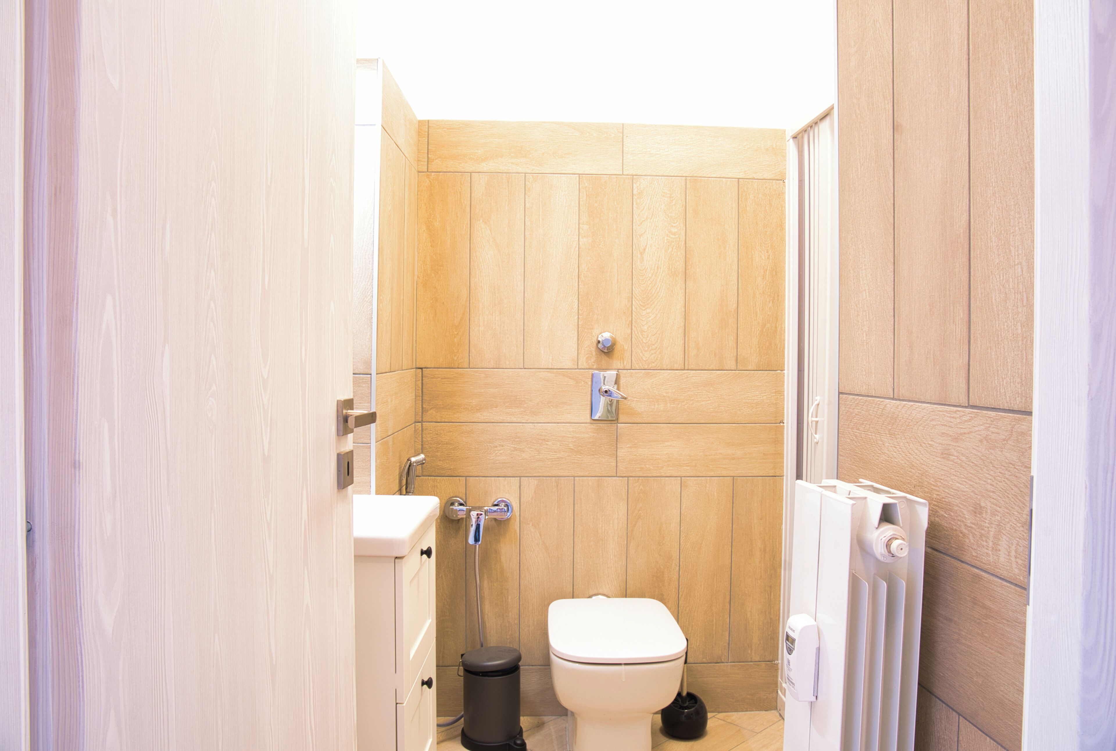 Une petite salle de bain compacte avec un mur en bois, des toilettes blanches, une poubelle noire et un radiateur blanc.