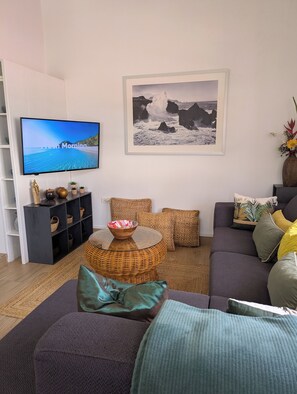 Una sala de estar con un sofá, televisión, un cuadro enmarcado y una mesita con un cuenco.