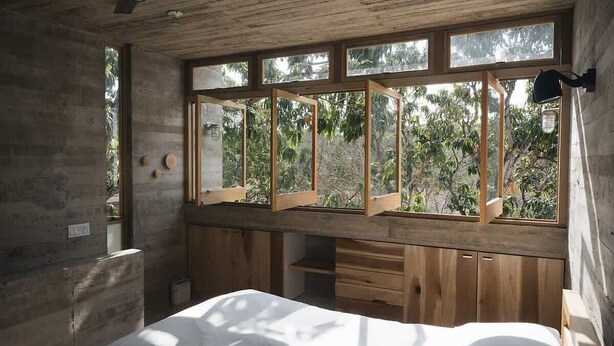 Un dormitorio con un ventanal grande, muebles de madera y vistas a zonas verdes.