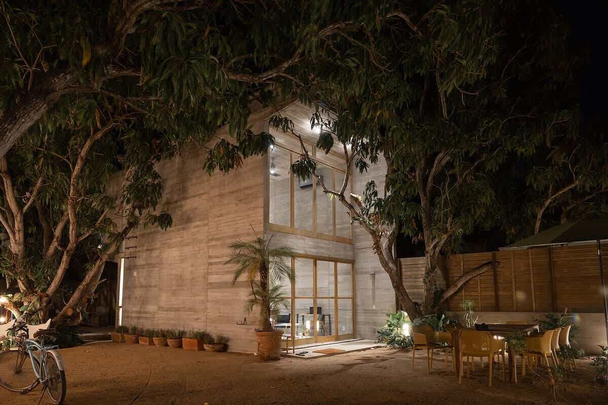 A modern building with large windows and a covered outdoor seating area surrounded by trees.