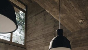 Un interior moderno con una pared de concreto, un sofá verde, una lámpara colgante y una obra de arte enmarcada.