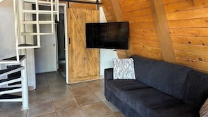 A cozy room with a wooden ceiling, a flat-screen TV mounted on the wall, a dark grey sofa, and a staircase leading to another area. - Charming Chalet with Kitchen and Scenic Views.  (Sedona)