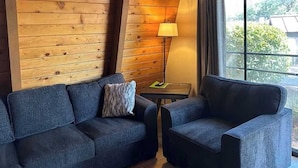 A room with a wooden wall, a sofa, a chair, a lamp, and a view through a window. - Charming Chalet with Kitchen and Scenic Views.  (Sedona)