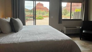 A hotel room with a large bed, a chair, and a view of red rock formations through the windows. - A stunning Pet-Friendly Studio facing the Red Rocks! (Sedona)