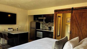 A hotel room with a bed, a small kitchenette, a dining area, and a sliding door. - A comfortable studio facing the breathtaking Red Rocks. (Sedona)