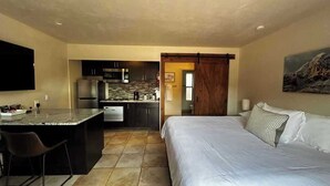A compact hotel room with a kitchenette, a bed, and a large window. - A comfortable studio facing the breathtaking Red Rocks. (Sedona)
