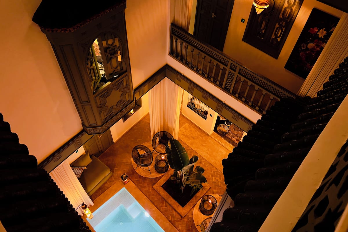 A high-ceilinged atrium with a central pool, a staircase with a balustrade, and a seating area with plants.