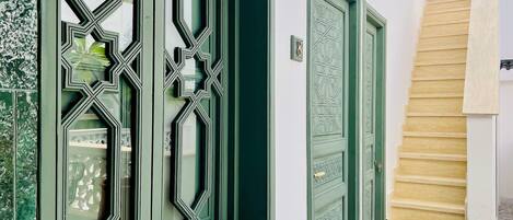 A green door with intricate geometric patterns, a white wall, and a wooden staircase.
