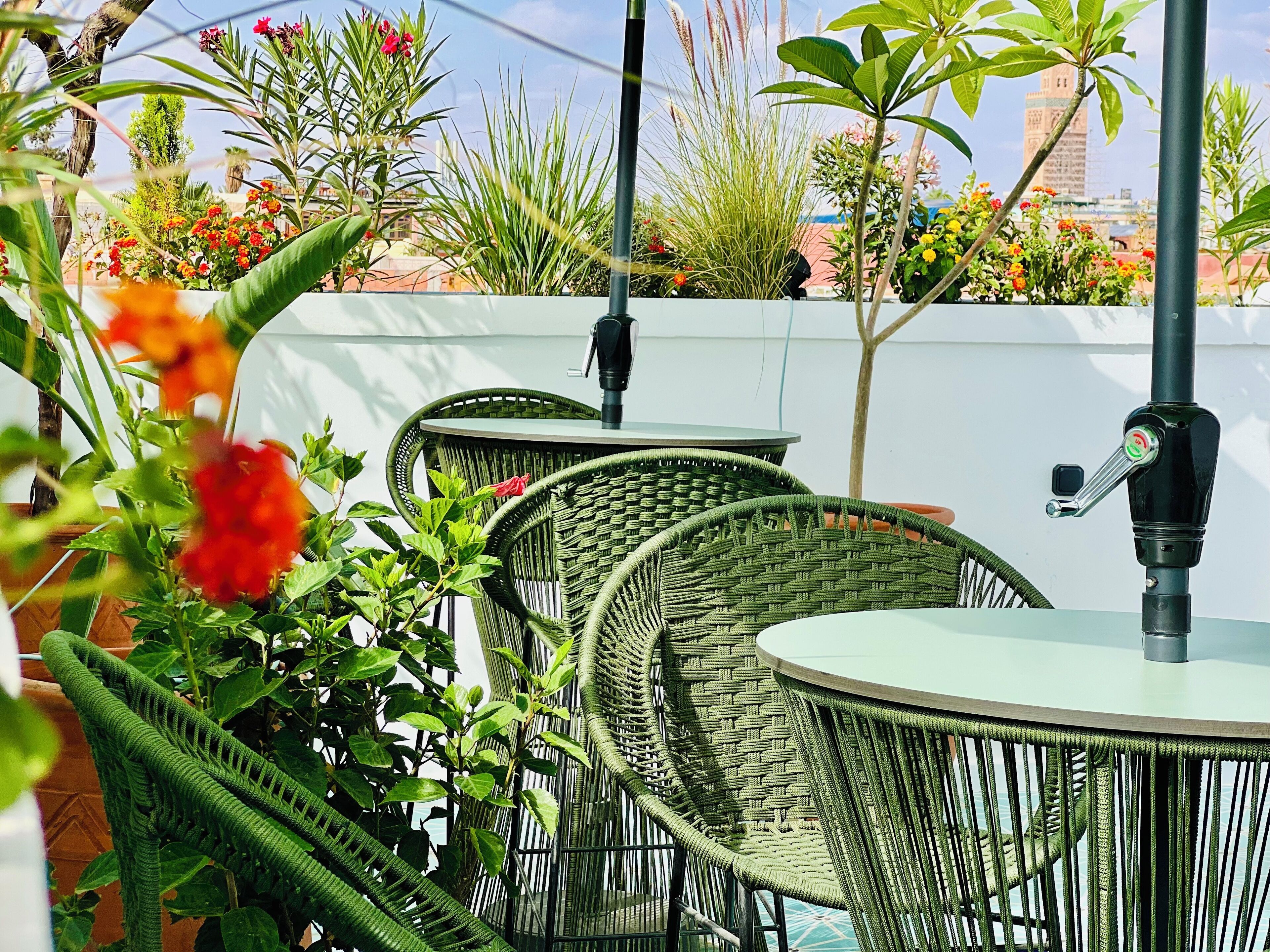 Outdoor wicker tables with attached umbrellas, surrounded by lush greenery and flowering plants.