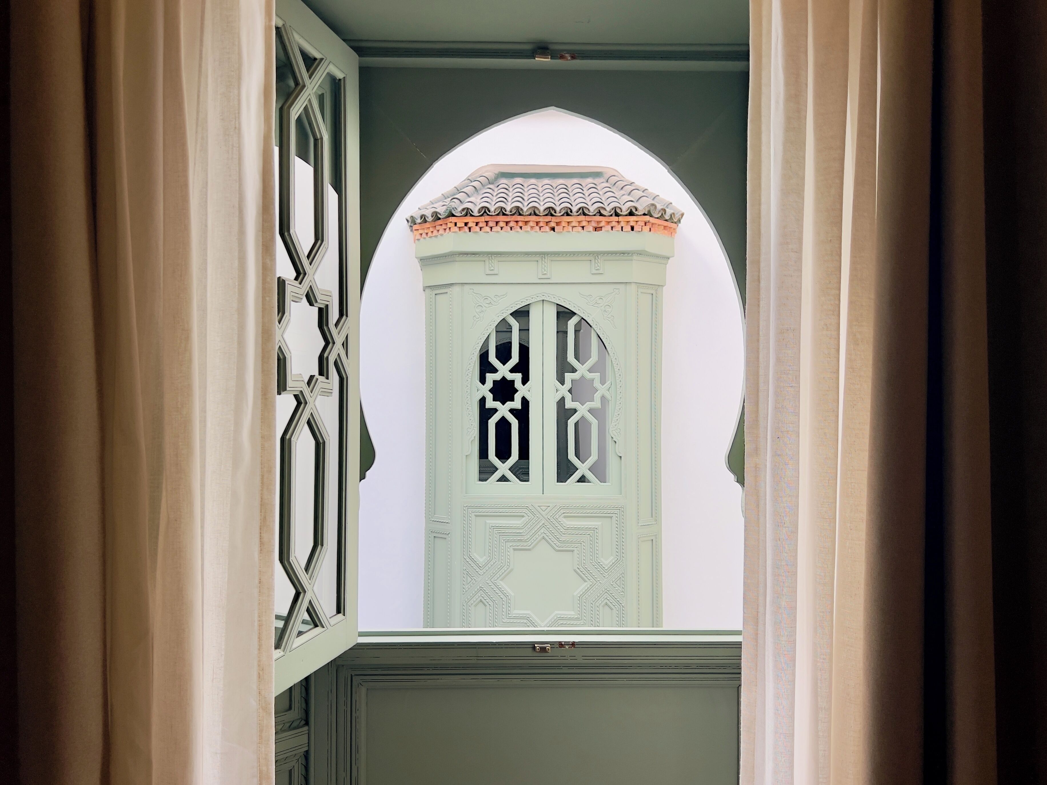 Une vue à travers une porte, avec un vitrail décoratif présentant des motifs géométriques et un toit recouvert de tuiles.