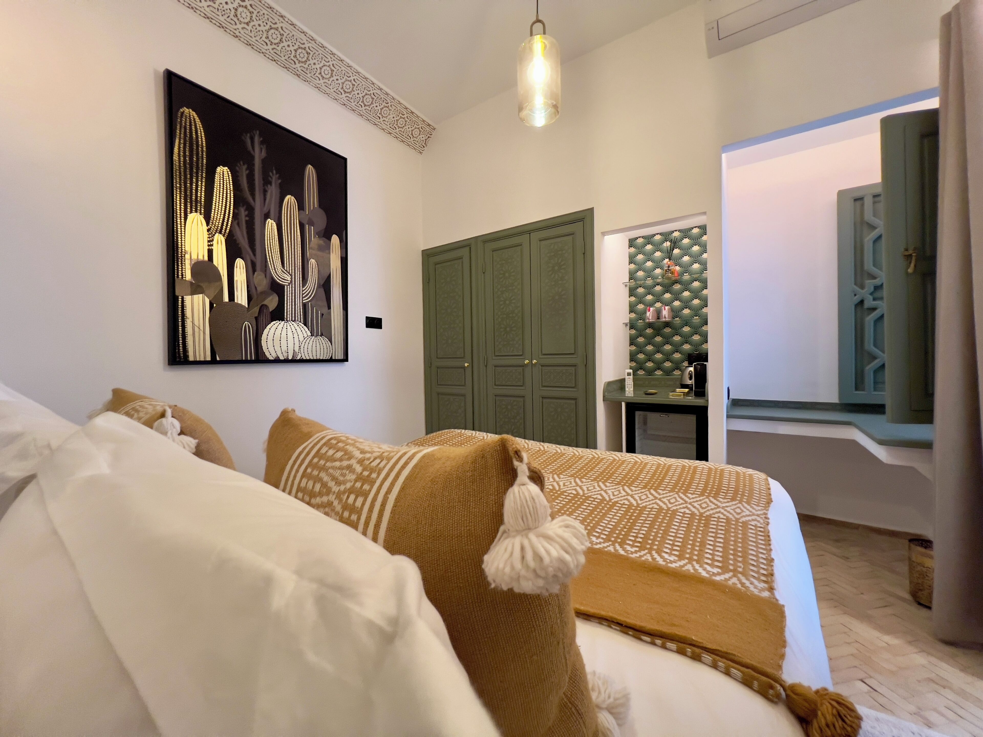 Un dormitorio con una cama, un armario verde, una obra de arte en la pared y una mesita de noche con una lámpara.