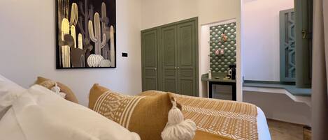 Un dormitorio con una cama, un armario verde, una obra de arte en la pared y una mesita de noche con una lámpara.