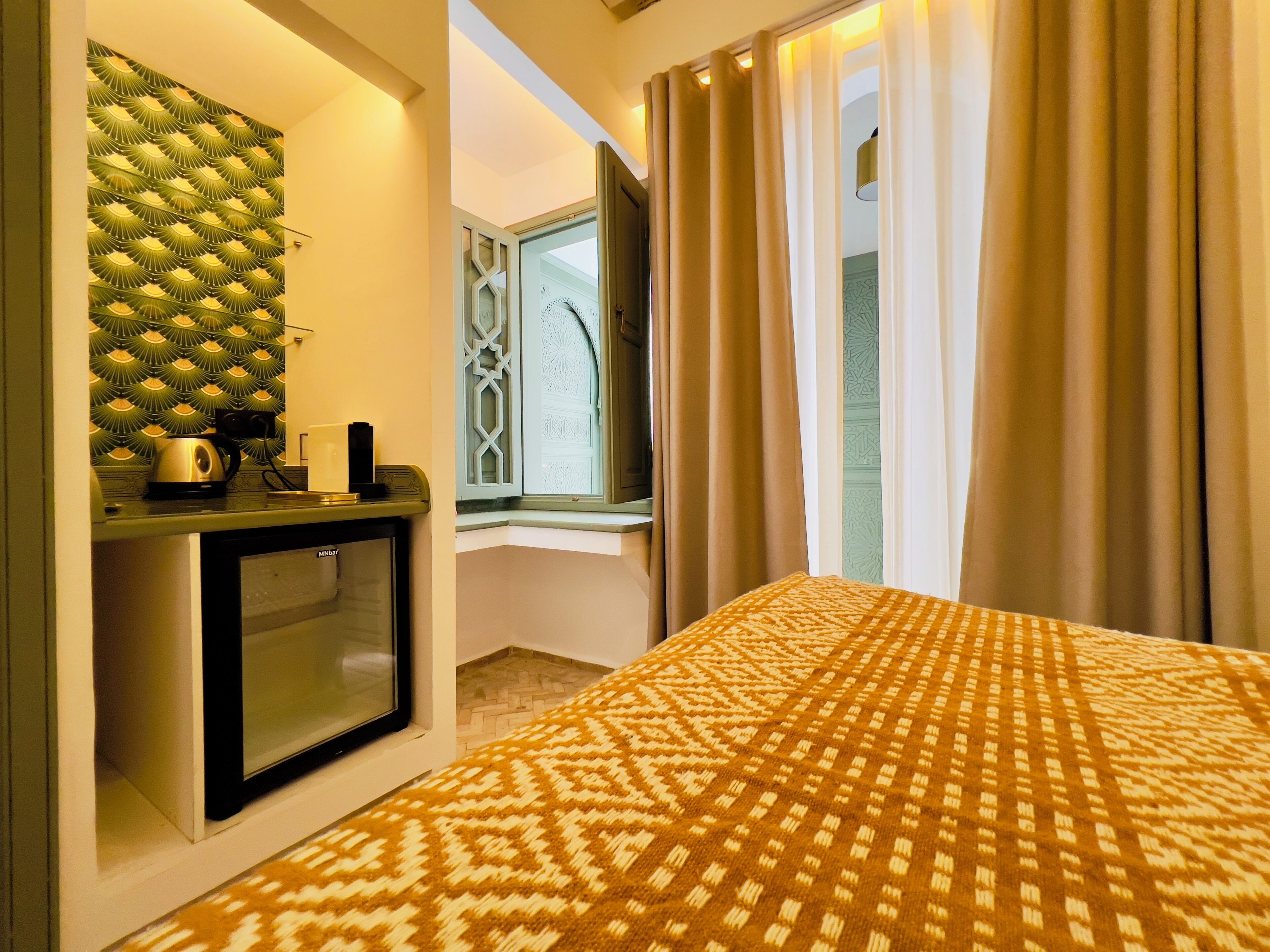 Habitación de hotel con cama, minibar, ventana con cortinas y pared con diseño.