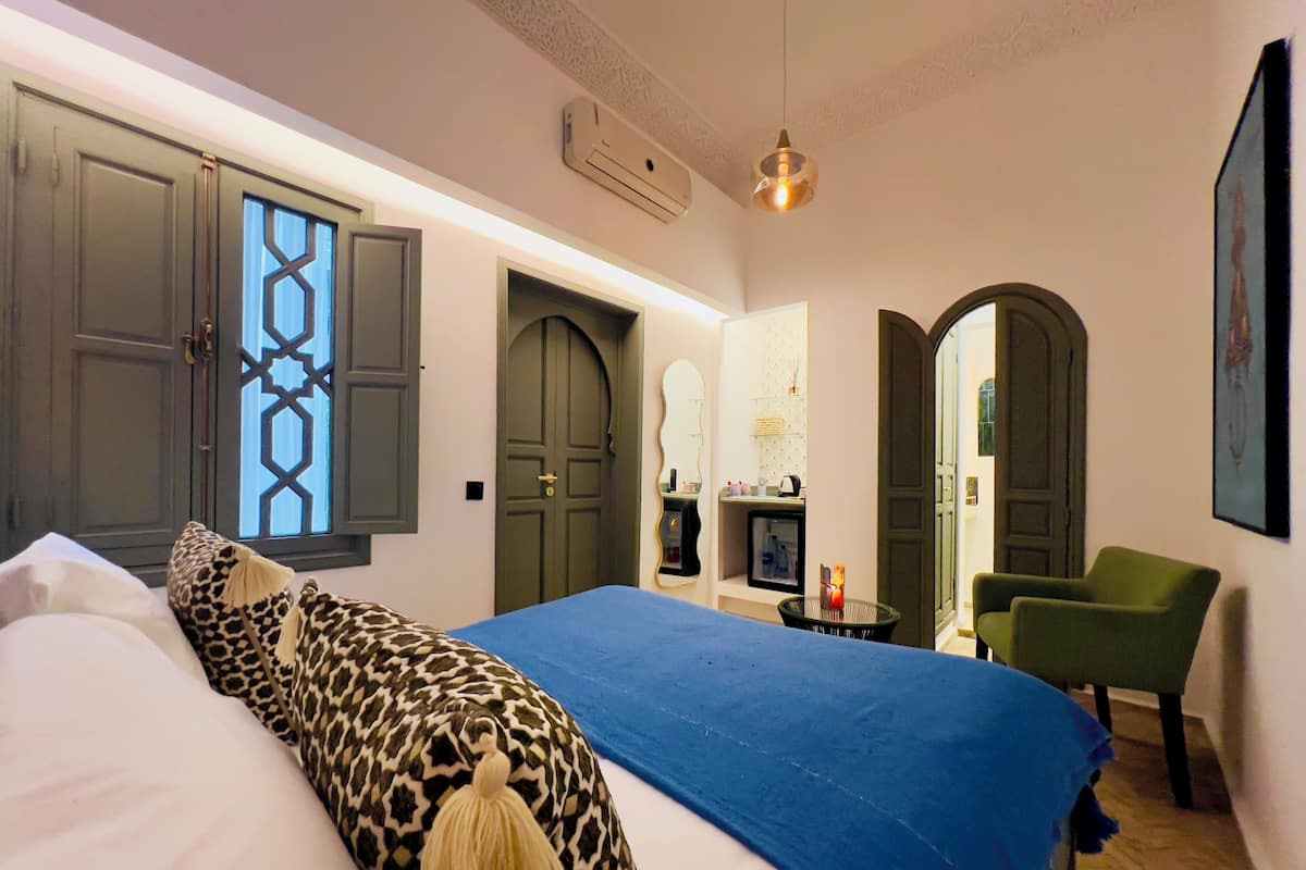 A bedroom with a large bed, a chair, a desk, and a wardrobe.