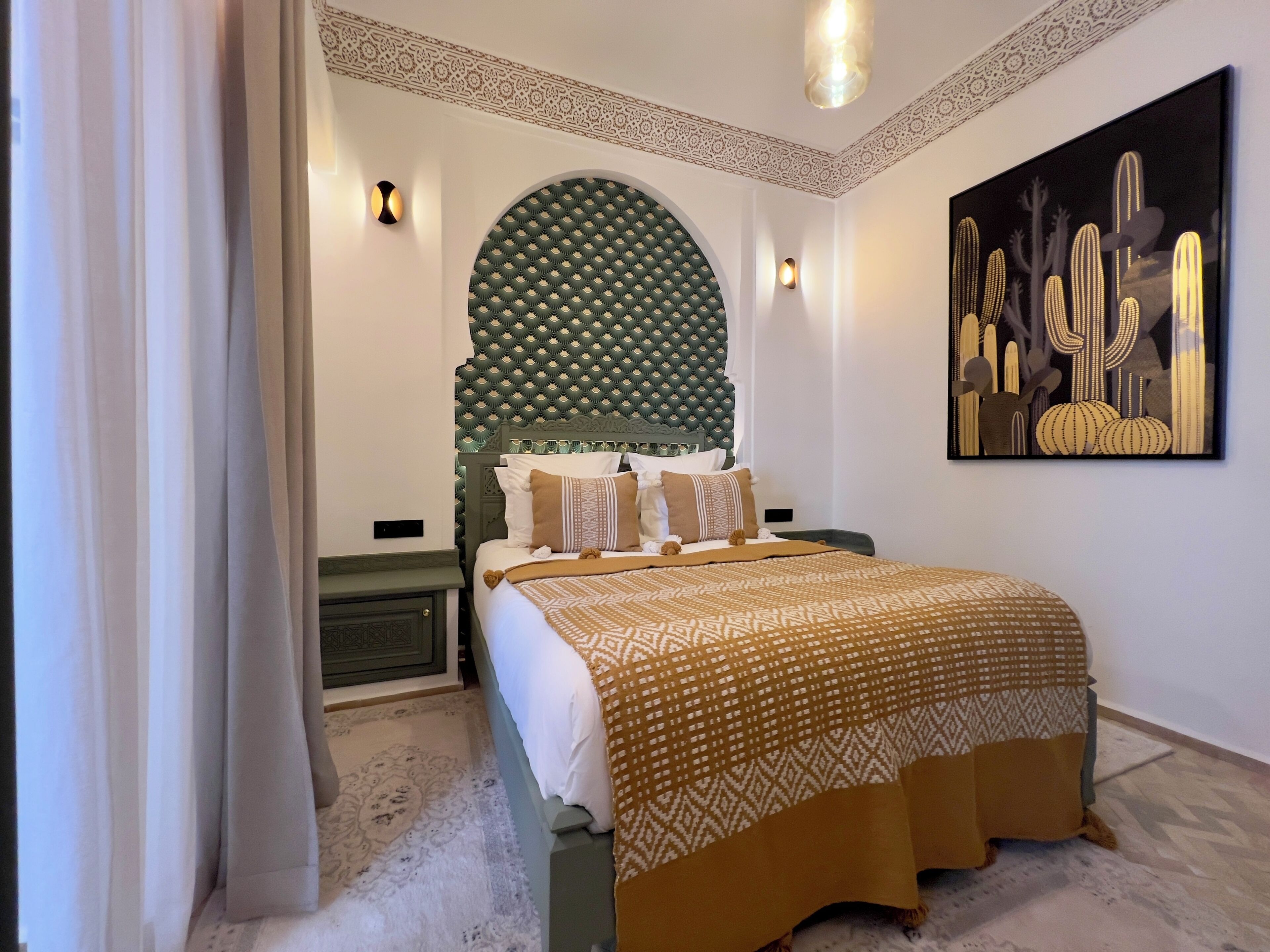 A modern bedroom with a patterned headboard, a large bed with patterned bedding, and a wall-mounted artwork of cacti.