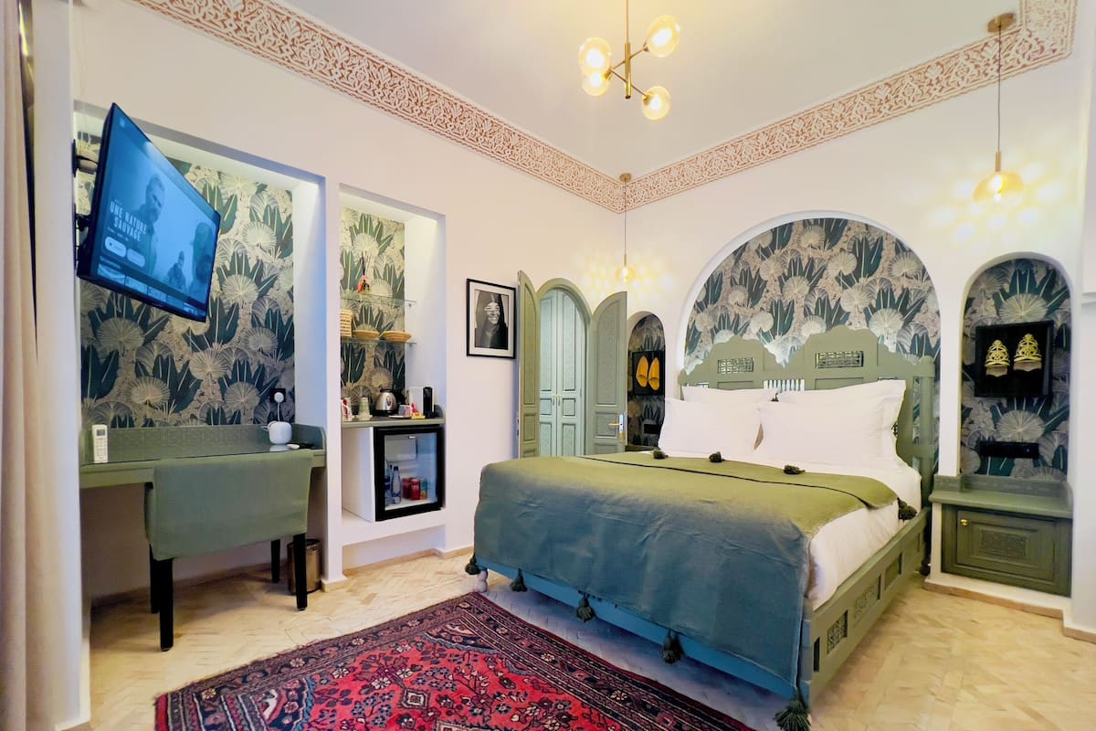 A bedroom with a bed, a desk, a television, and decorative wall art.