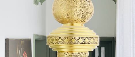 Un lustre doré suspendu, orné de motifs complexes, une porte verte aux motifs géométriques et un tableau floral accroché au mur.