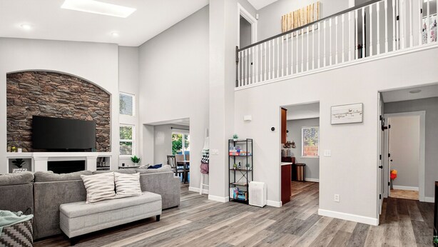 A spacious living room with a stone accent wall, a flat-screen TV, a grey sectional sofa, and a wooden floor.