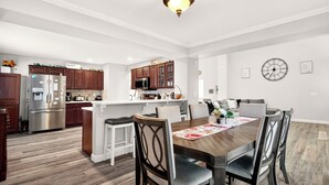 A modern kitchen with wooden cabinets, a stainless steel refrigerator, and a dining area with a wooden table and chairs.