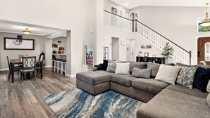 A spacious living room with a large sectional sofa, a dining area with a wooden table and chairs, and a staircase leading to an upper level.