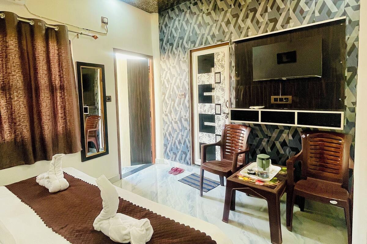 A hotel room with a bed, a TV, a seating area, and a patterned wall.