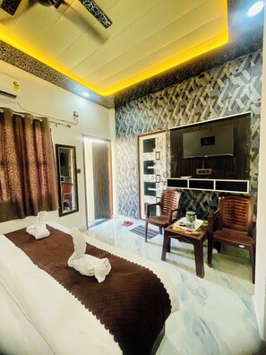 A hotel room with a bed, a TV, a seating area, and a patterned wall. - Hotel Kashi In (Varanasi)