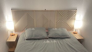 Ein Bett mit geometrischem Kopfteil, zwei Nachttischlampen und einer grauen Tagesdecke.
