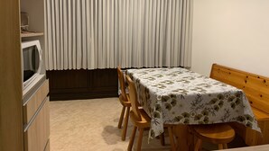 Ein Zimmer mit Esstisch, Stühlen, einer Holzbank, einer Mikrowelle und einem Fenster mit Vorhängen.