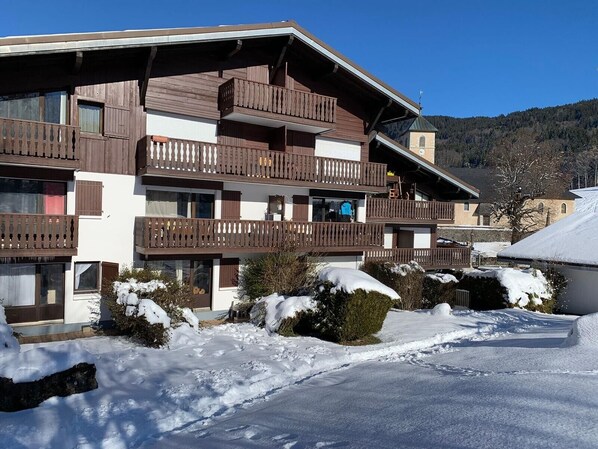 A multi-story building with balconies, a ski lift tower, and snow-covered surroundings.