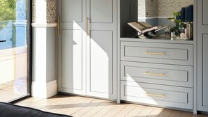 A modern room with a large grey wardrobe, a small desk with a lamp, and a view of the outdoors through a sliding glass door. - Thames Mansion - River View (Windsor)