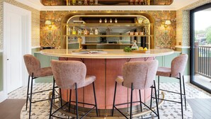 A bar area with a curved counter, three bar stools, and a variety of bottles and glasses. - Thames Mansion - River View (Windsor)