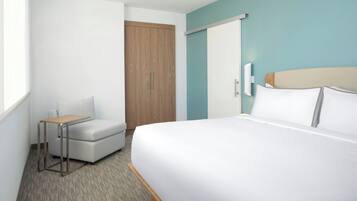 Una habitación de hotel con cama, una mesita, una silla, un armario y una ventana.