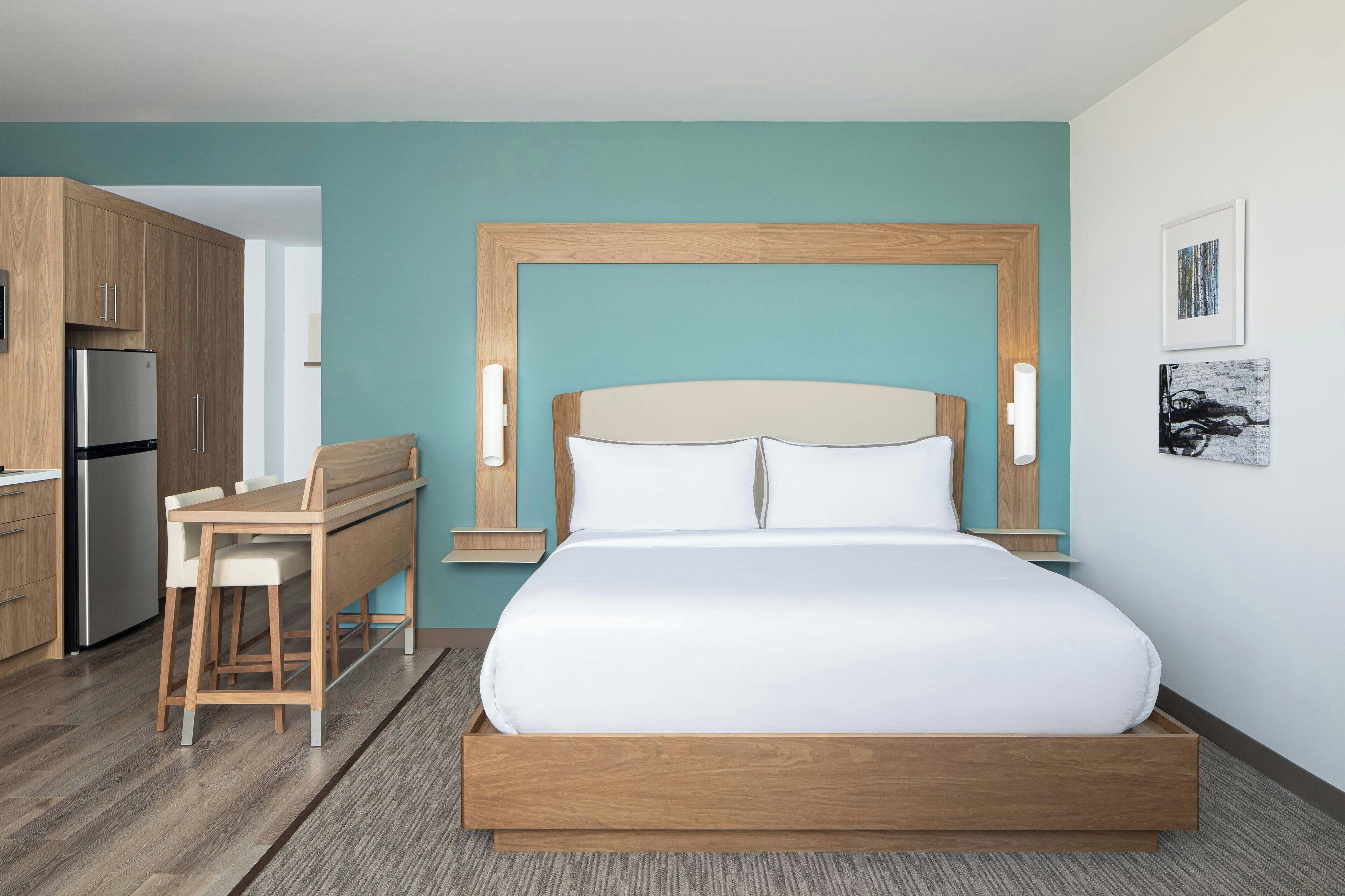 Ein modernes Hotelzimmer mit einem Bettgestell aus Holz, einem Schreibtisch und einer Küchenzeile.