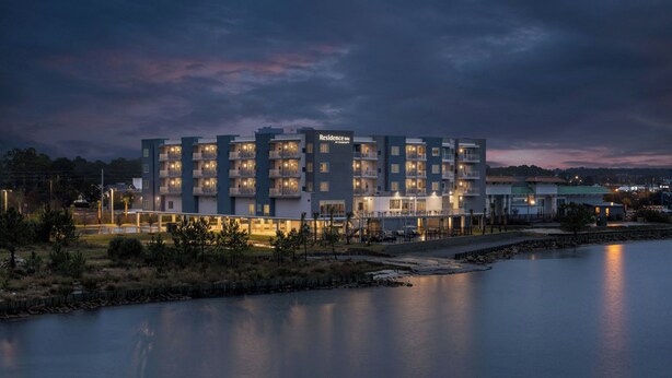 A multi-story hotel with balconies, a swimming pool, and a waterfront view.