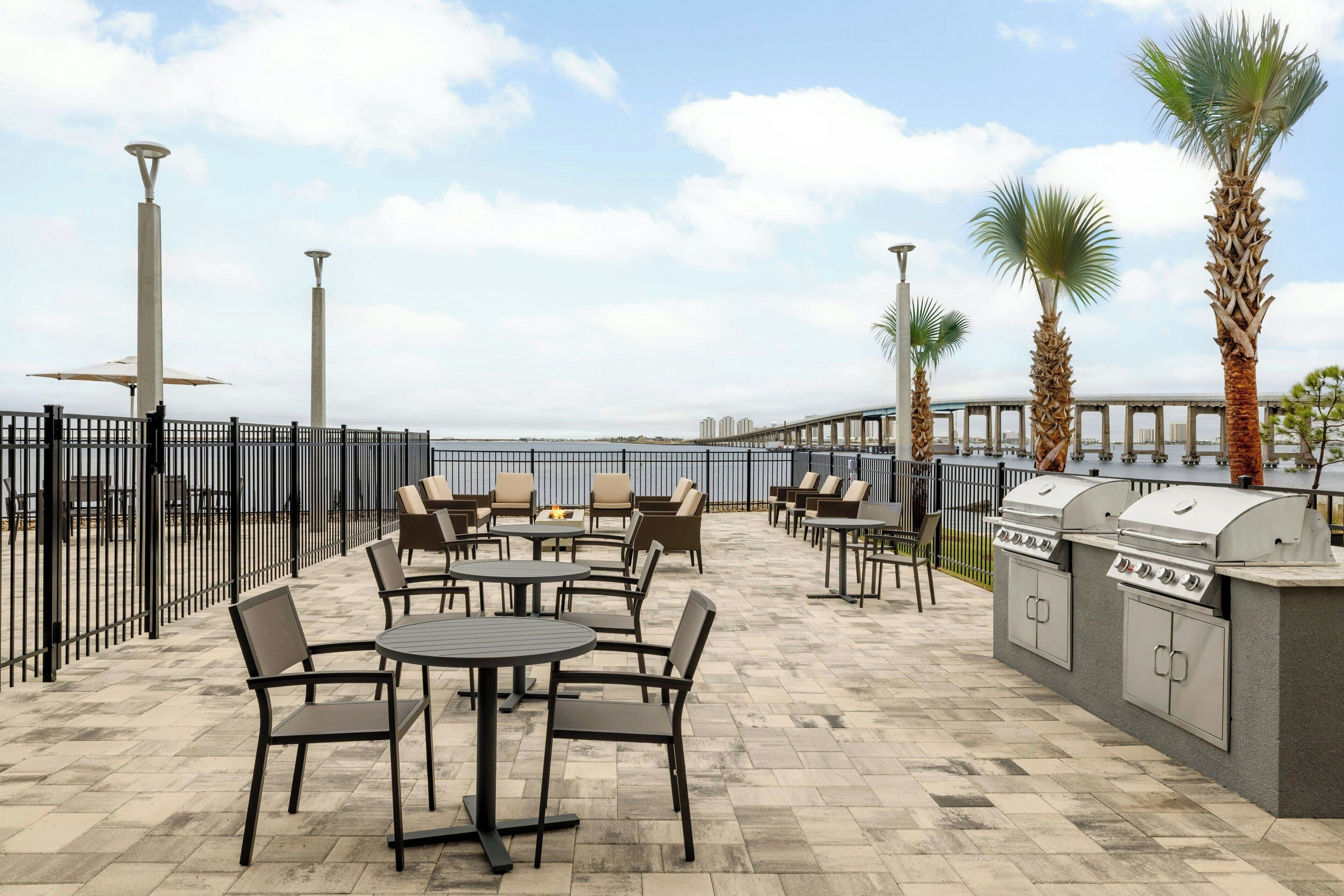 An outdoor patio with round tables and chairs, a grill station, and a view of the sea.