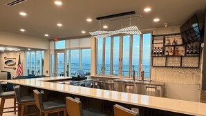 A modern bar area with a long counter, bar stools, and a view of the ocean through large windows.