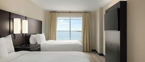 A hotel room with two beds, a large flat-screen TV, a nightstand, and a view of the sky.
