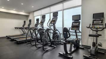 Et fitnesscenter med løbebånd, crosstrainere og romaskine, med store vinduer og udsigt til himlen.