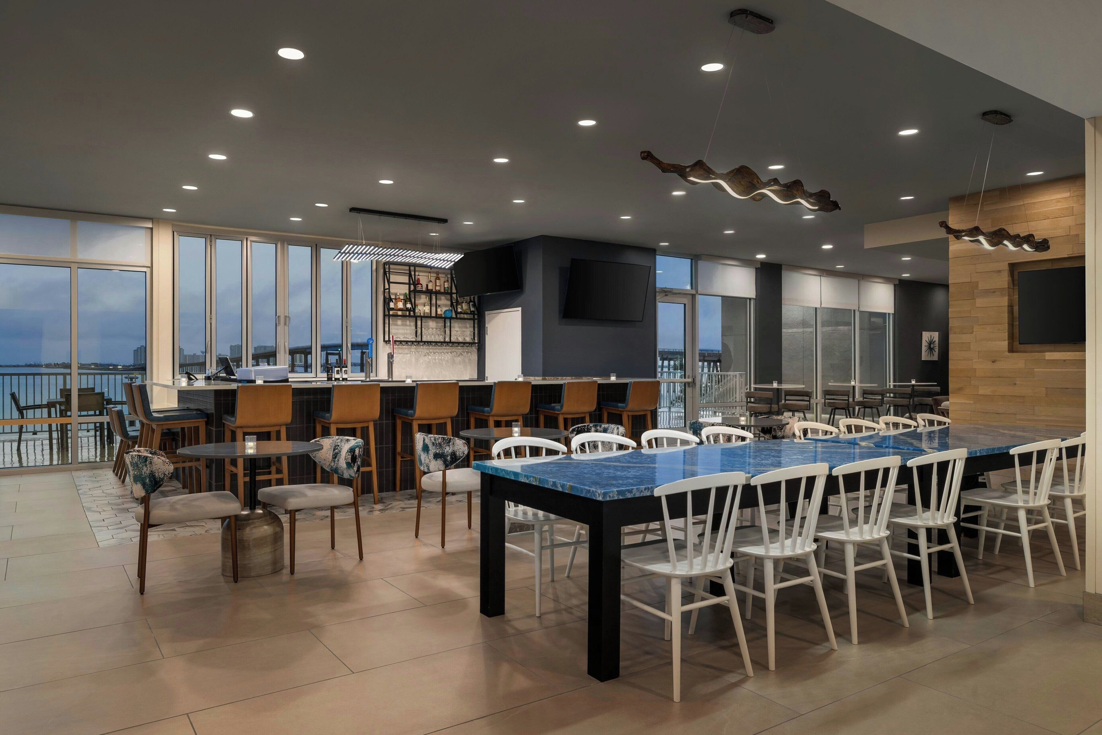 A modern restaurant with a large dining area, high ceilings, and large windows offering views of the city.