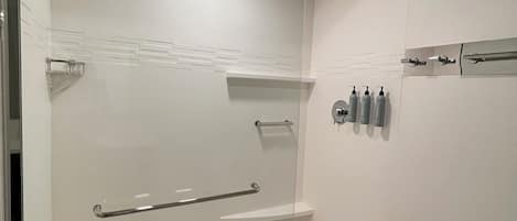 A modern bathroom with a glass shower enclosure, a handrail, and a shelf with toiletries.
