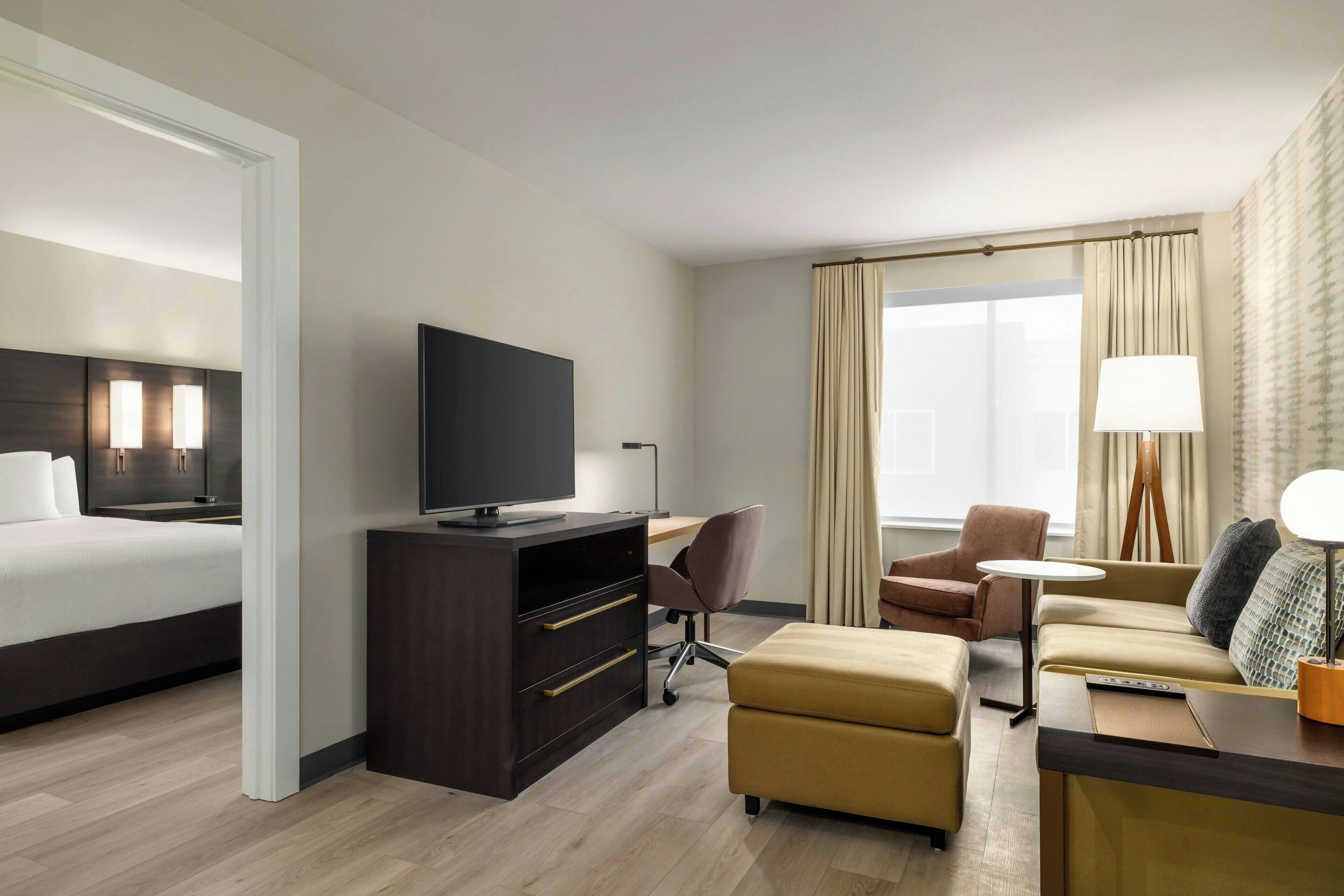 A hotel room with a bed, a desk, a television, a sofa, and a lamp.