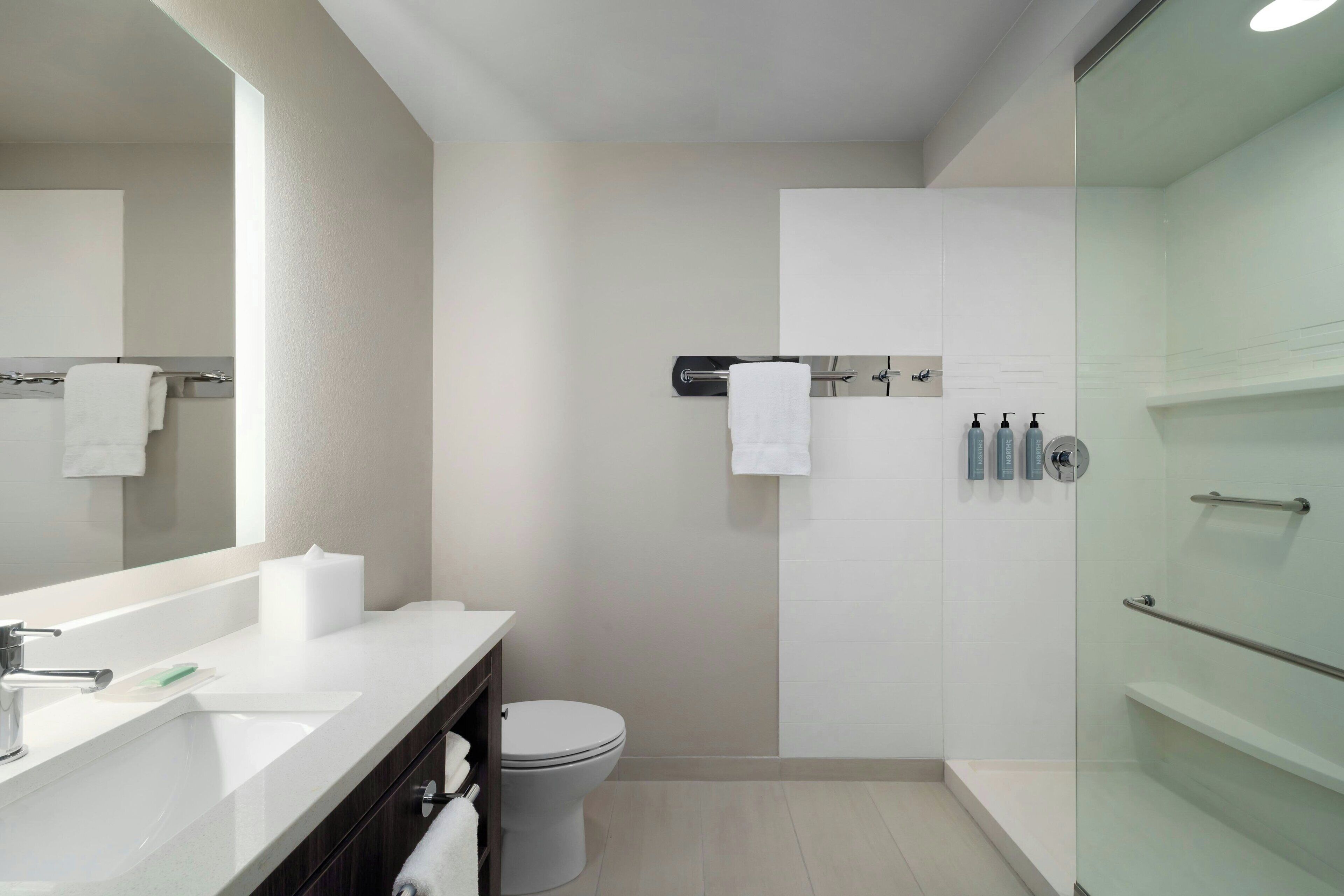A modern bathroom with a large mirror, white sink, and a glass shower enclosure.