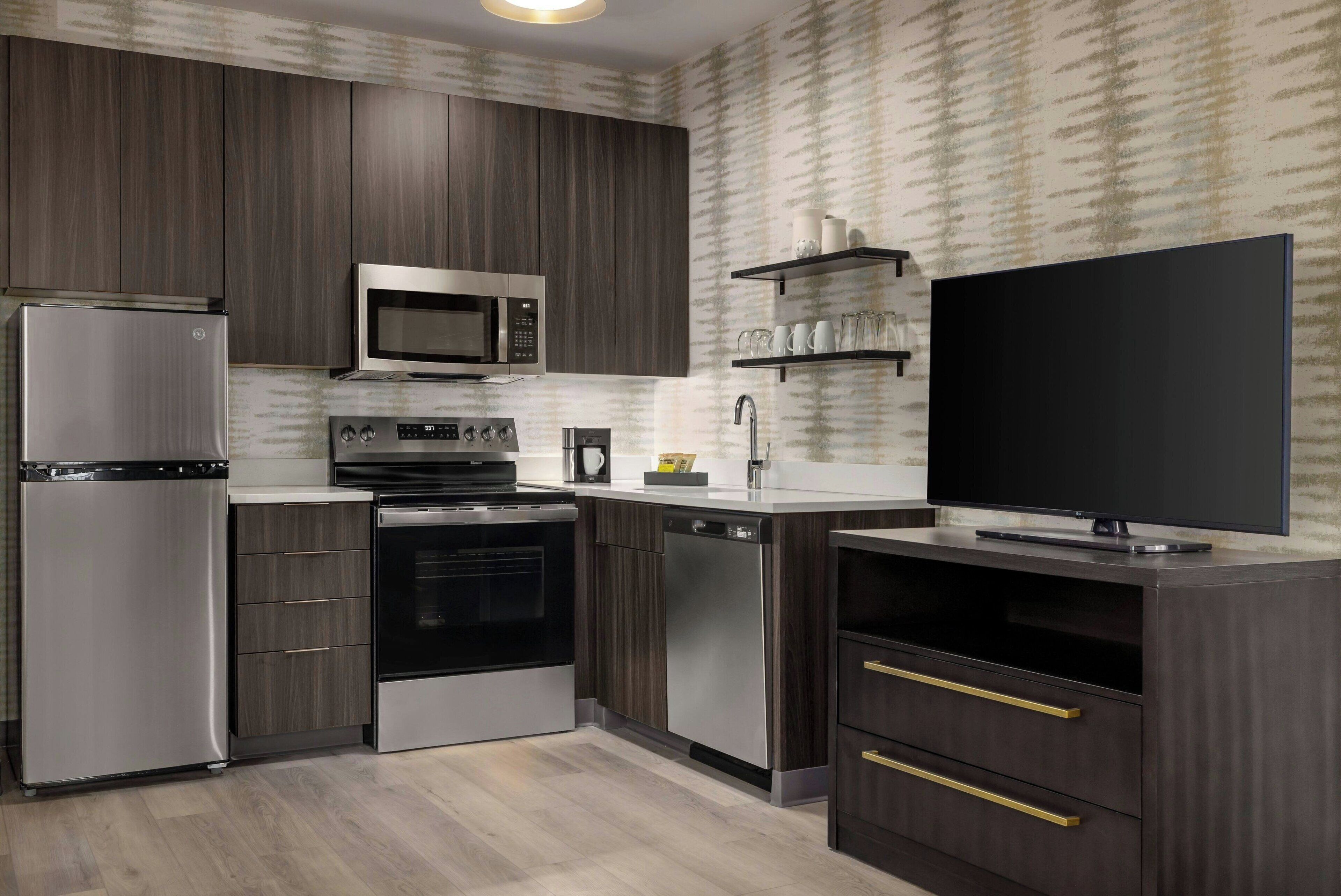 A modern kitchen with stainless steel appliances, dark wood cabinets, and a flat-screen TV.