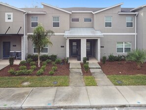 A two-story residential building with a front porch, a small garden area, and a visible mailbox.